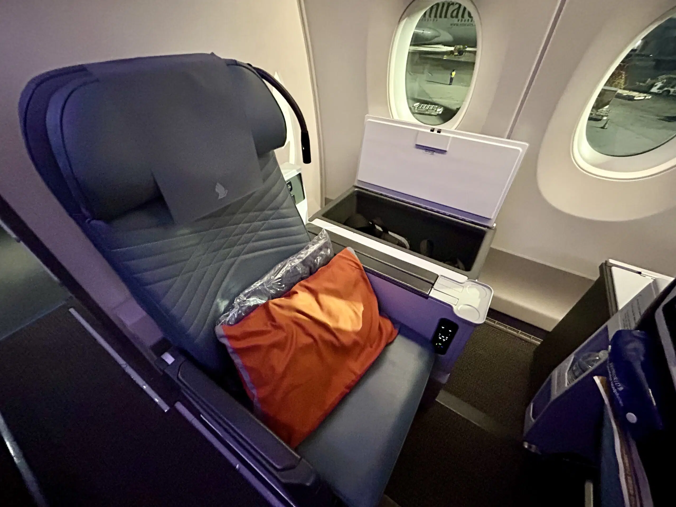 an empty airplane seat with an orange pillow 