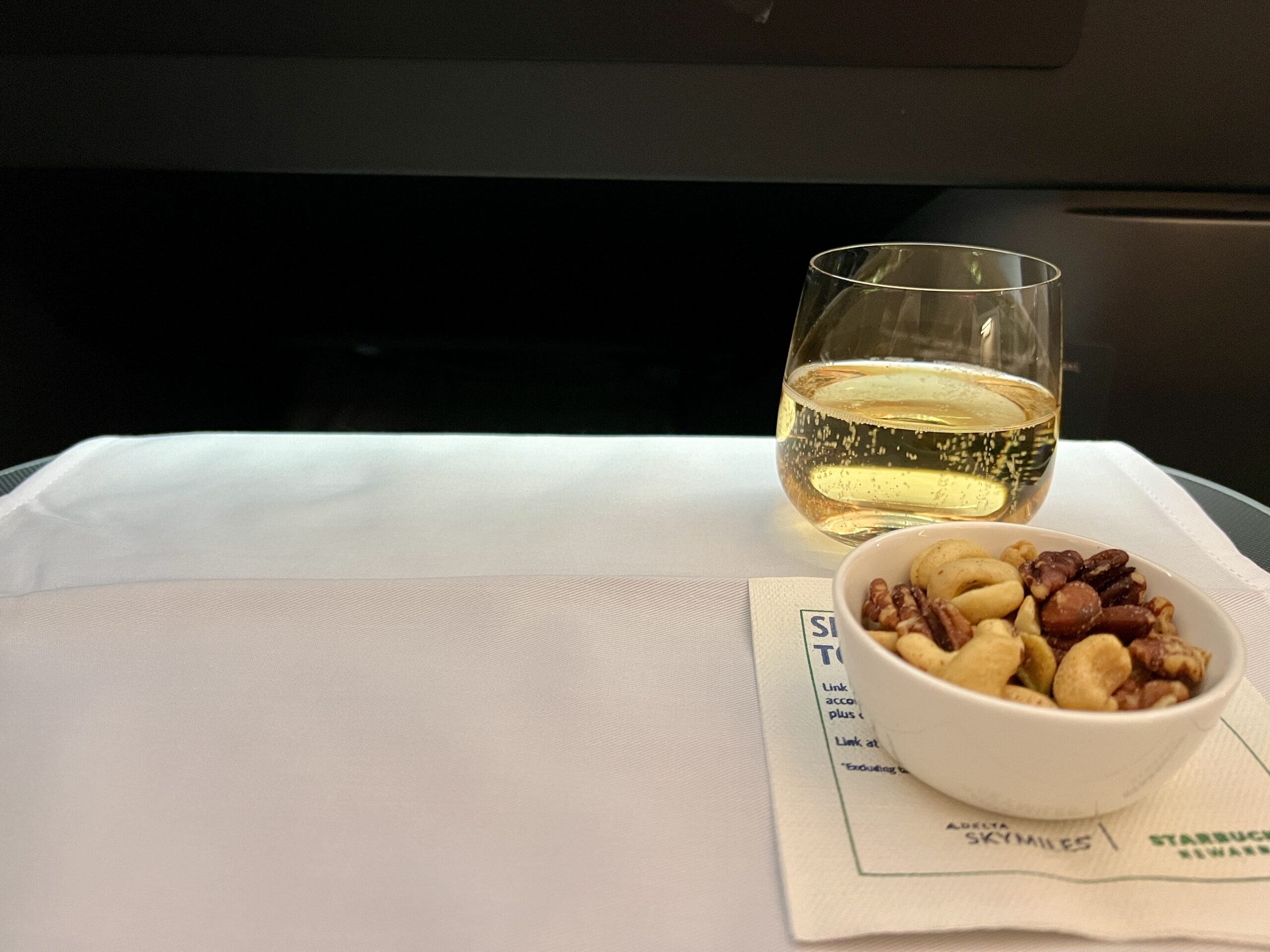 a glass of champagne and mixed nuts on an airplane tray