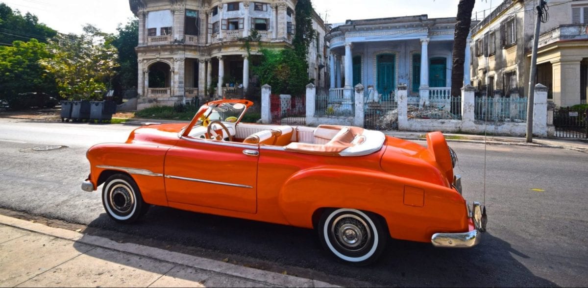 An orange car parked on the side of a building in Cuba